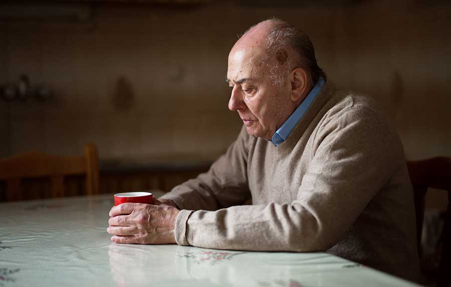 un señor está solo en el living de su casa tomando un café